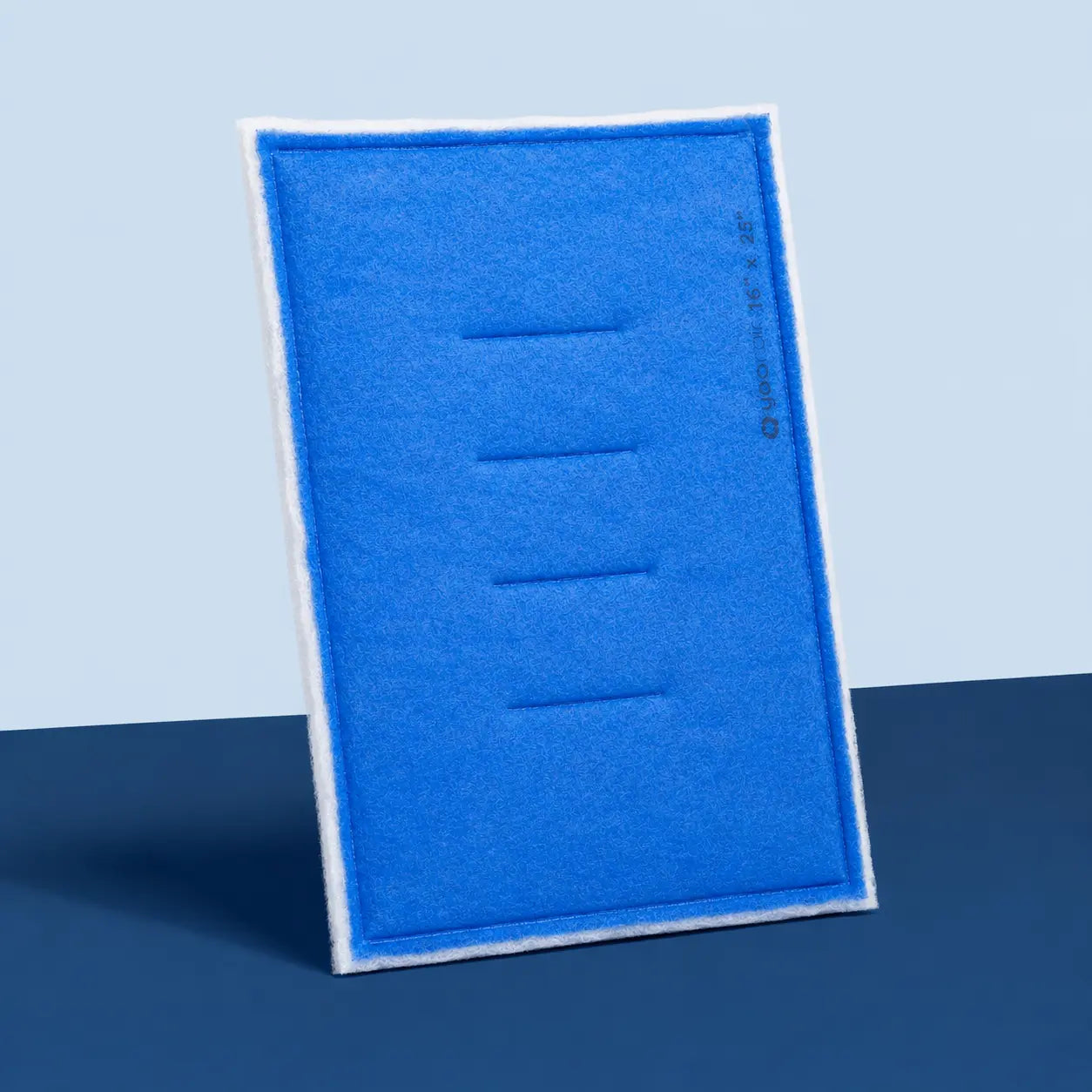 A rectangular blue filter pad with a white border, standing upright on a dark blue surface against a light blue background.