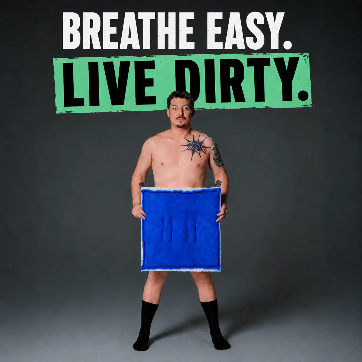 A shirtless man with tattoos stands against a dark gray studio background holding a bright blue square cloth. Large text at the top reads 'BREATHE EASY.